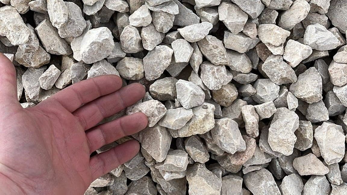 Avuç içinde tutulan 12-22 mm mıcır taneleri, arkada mıcır yığını